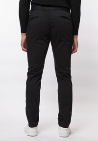 Zwarte broek van gladde stof, met een slim fit, zij- en achterzakken, en een schone, minimalistische stijl. Gedragen met witte schoenen.