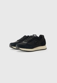 Schwarze Sneaker aus einer Mischung von Wildleder und Stoff, mit einer runden Zehenpartie, strukturiertem Seitenpanel und einer beigen Gummisohle.