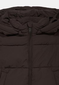 Καφέ μπουφάν με ψηλό γιακά, μπροστινό φερμουάρ και οριζόντιες ραφές. Το ύφασμα φαίνεται μαλακό και λείο, παρέχοντας μόνωση.