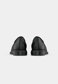 Paire de chaussures habillées en cuir noir vues de dos sur un fond uni gris clair.