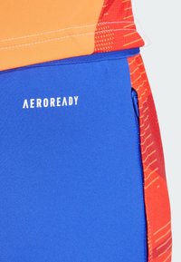 AEROREADY Sportbekleidung mit einem orange-rot gemusterten Oberteil und einer einfarbigen blauen Hose, hergestellt aus leichtem, feuchtigkeitsableitendem Material.