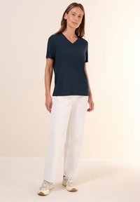 Námořnický v-neck tričko z měkké tkaniny, spárované s bílými rovnými kalhotami a světlebarevnými teniskami. Jednoduchý design, volný střih, krátké rukávy.