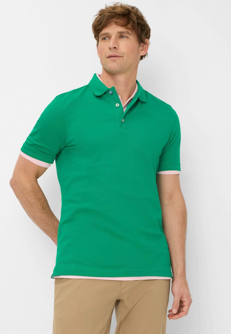 Polo vert avec un design classique, présentant une patte de boutonnage à deux boutons, un accent rose sur les manches et une texture douce et lisse.