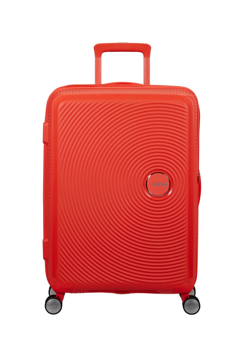 Valigia rigida rossa con motivi a cerchi concentrici, manico telescopico, quattro ruote girevoli e un logo rotondo sulla parte anteriore.