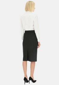Czarna spódnica ołówkowa z teksturowanym wzorem, długości do kolan, z rozporkiem po bokach, zestawiona z białą koszulą z długim rękawem i czarnymi szpilkami.