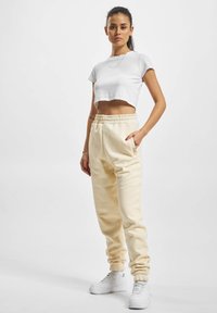 Tricou alb scurt, pantaloni de trening crema cu talie și manșete elastic, buzunare laterale, asortați cu adidași albi.
