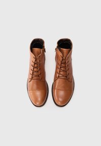 Bottines en cuir marron avec un bout arrondi, un laçage à l'avant et une fermeture à glissière sur le côté. Texture lisse avec des détails matériels minimaux.