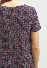Abito a fantasia navy con design geometrico in rosso e blu, maniche corte e apertura a chiave sul retro con chiusura a bottone.