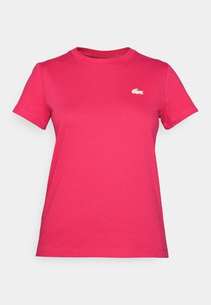 Rózsaszín pamut póló rövid ujjakkal és kerek nyakkivágással. A bal mellrészen egy kis fehér Lacoste logó található.