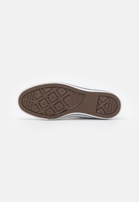 Hnedá gumová podrážka s diagonálnymi a geometrickými vzormi, s bielymi okrajmi. Text "Converse All Star" je vytlačený blízko päty.