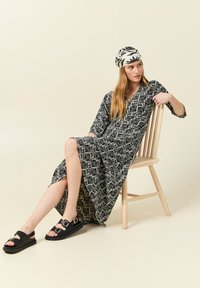 Schwarz-weißer gemusterter Maxikleid mit Dreiviertelärmeln, ausgestattet mit einem gespaltenen Rock, kombiniert mit schwarzen Sandalen und einem passenden Kopfband.