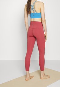 Reggiseno sportivo blu chiaro con spalline incrociate, abbinato a leggings rosa alti in vita e aderenti. Il tessuto sembra liscio con dettagli minimi.
