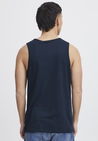 Námornícky modrý bezrukávový top vyrobený z mäkkého materiálu, s okrúhlym výstrihom a voľným strihom. Bez vzorov alebo viditeľných kovových detailov.