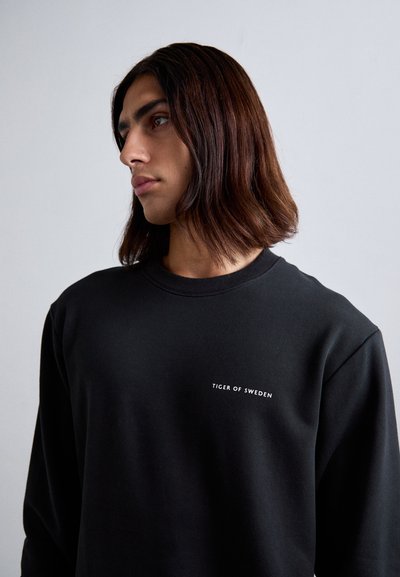 Black sweatshirt made of soft material with round neckline, featuring white text "TIGER OF SWEDEN" embroidered on the chest.