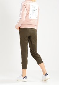 Ljusrosa sweatshirt med grafisk tryck på baksidan, kombinerad med olivgröna cropped byxor och vita sneakers med blå accenter.