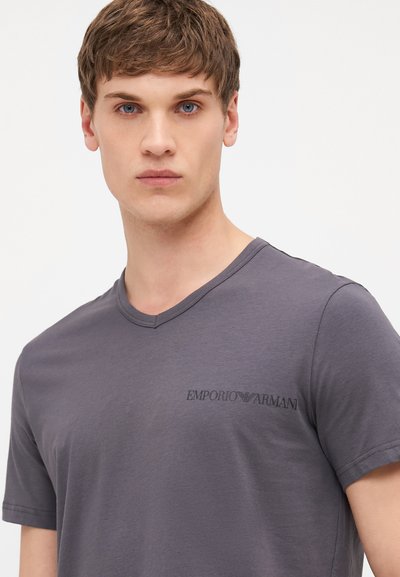 Šedé tričko s krátkým rukávem a výstřihem do V vyrobené z měkké tkaniny, na hrudi s černým logem "Emporio Armani". Hladká textura a volný střih.