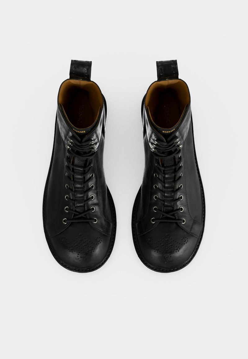 Paar schwarze Leder-Schnürstiefel mit perforiertem Design an den Zehen und Zuglaschen an der Ferse, aus der Vogelperspektive auf weißem Hintergrund dargestellt.