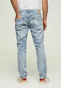 Vaqueros de mezclilla azul claro con corte ajustado, que cuentan con dos bolsillos traseros y una etiqueta de cuero en la cintura. Combinados con zapatillas blancas.