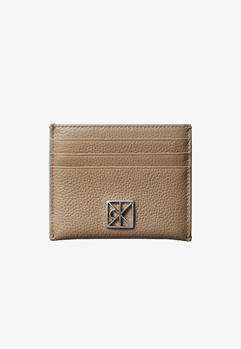 Porte-cartes en cuir beige texturé avec trois emplacements pour cartes et un petit logo métallique géométrique argenté sur le devant.