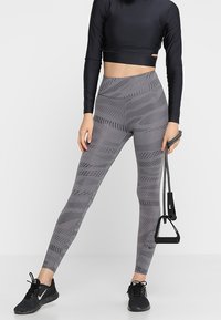 Leggings grigi con un motivo testurizzato di linee e punti, design a vita alta, abbinate a un crop top nero e scarpe da ginnastica nere.