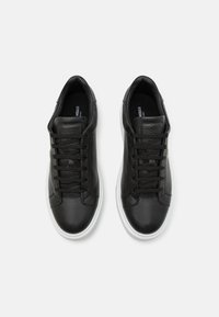 Zapatillas de cuero negro con parte superior texturizada, suela de goma blanca y cierre tradicional con cordones. Diseño minimalista sin adornos.