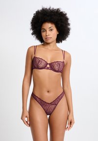 Ensemble soutien-gorge et string en dentelle violette avec motif floral, tissu transparent, bretelles ajustables et bordures festonnées pour un design délicat.