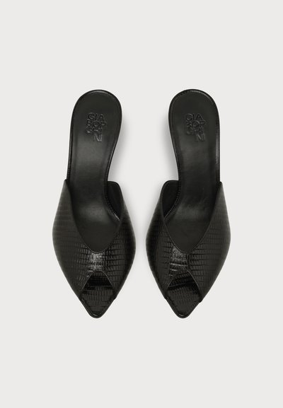 Paire de mules noires en cuir texturé à bouts ouverts, à enfiler, avec bouts pointus et semelles plates sur fond blanc.