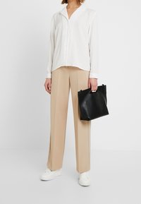 White button-up shirt with a soft texture, beige wide-leg trousers, and a black leather tote bag with a minimalist design. White sneakers featured.