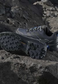 Σκούρα γκρι παπούτσια πεζοπορίας Adidas Terrex με ανθεκτικές σόλες Continental τοποθετημένα σε βραχώδες έδαφος.