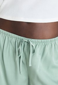 Pantalons à cordon de serrage vert clair avec une texture lisse, présentant une taille élastique et un accent en nœud lié.