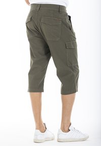 bermudas cargo couleur kaki avec plusieurs poches, longueur genou, en tissu résistant, dotées d'une coupe décontractée et d'ourlets retroussés, portées avec des baskets blanches.