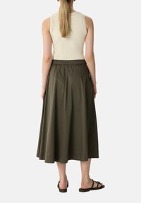 Ärmelloses cremfarbenes Top mit strukturierten Details, kombiniert mit einem fließenden, olivgrünen Midikleid mit elastischem Bund und glatter Oberfläche.