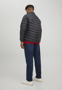 Giacca a vento grigia scura con cuciture a zigzag, dotata di colletto rialzato. Abbinata a jeans in denim blu e sneakers bianche.