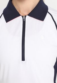 Biała koszulka polo z czarnym kołnierzykiem i zamkiem błyskawicznym z przodu, z delikatnym logo na lewej piersi i czarnymi szwami wzdłuż szwów ramion.