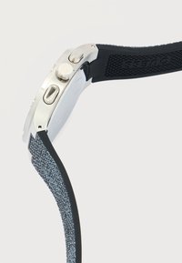 Vue latérale d'une montre-bracelet en argent avec un bracelet texturé bleu-gris et noir, et trois boutons de contrôle sur le côté du boîtier de la montre.