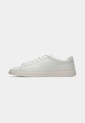 White leather sneaker with a smooth texture, rounded toe, flat rubber sole, and minimal lacing. Subtle branding on the side and heel.