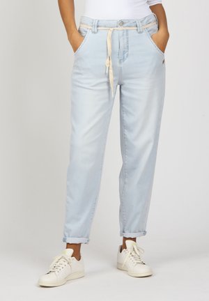 Light blue denim pants with a relaxed fit, rolled cuffs, drawstring waistband, and two front pockets. Worn with white sneakers.