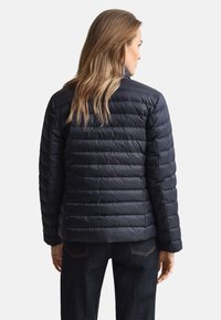 Sort dunjakke med quiltet design og høj krave, med en strømlinet form og blød tekstur. Synlige syninger og minimalt hardware.