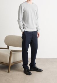 Grau Crew-Neck-Pullover, marineblaue Hose und schwarze Schnürschuhe. Glatte Textur, schlichtes Design und standardmäßige Passform. Neutraler Hintergrund.
