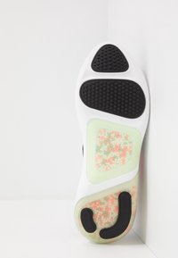 Suela de una zapatilla con una superficie blanca, acentos de goma negra, zonas de agarre texturizadas, secci�ón translúcida verde con cuentas de colores.