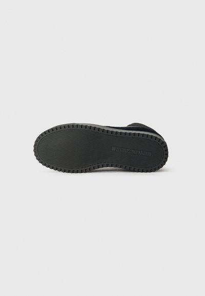 Botte en daim noire avec une semelle en caoutchouc texturé. La semelle présente de profonds sillons pour une meilleure adhérence, et le design possède un bout rond.