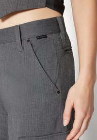 Spodnie w szary wzór w warkocz z dopasowaną talią, płaską przednią kieszenią oraz widoczną etykietą z logo blisko pasa.