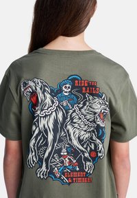 Dos grandes perros rugientes encadenados, una figura esquelética vestida de azul, un conejo de dibujos animados corriendo sobre las vías del tren, con el texto "Montar en las vías" y "Elemento y Madera!".