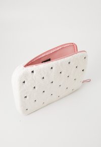 Faux fur white pouch with pink lining, featuring small black embroidered dots, rectangular shape, zip closure, and a looped handle.