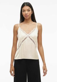 Silkekamisol i lyst beige med blonder. Har tynne justerbare stropper og V-utringning. Myk tekstur med avslappet passform.