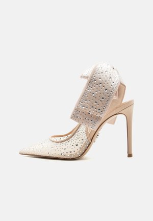 Chaussure beige à talon haut et bout pointu ornée de strass étincelants et d'un grand nœud décoratif sur la bride de cheville.