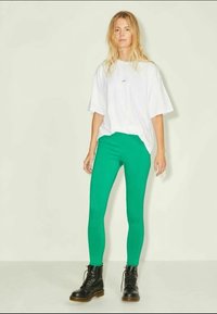 Πράσινα κολάν, εφαρμοστού σχεδιασμού, ελαστικό υλικό, συνδυασμένα με μια υπερμεγέθη λευκή μπλούζα. Μαύρες μπότες με κορδόνια ολοκληρώνουν την εμφάνιση.