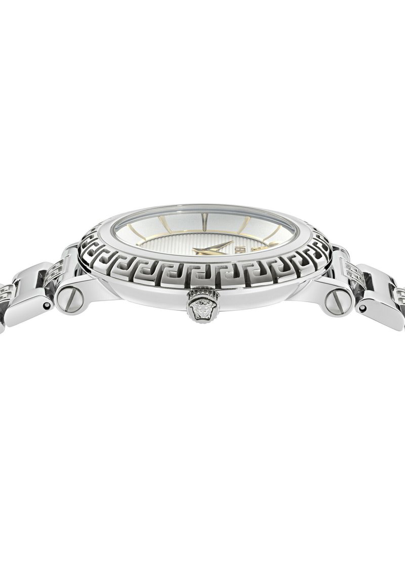 Silberne Armbanduhr mit Lünette im griechischen Schlüsselmotiv, silbernen und goldenen Zeigern sowie einem strukturierten weißen Zifferblatt, seitlich dargestellt.