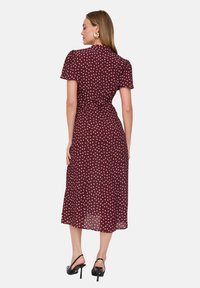 Dunkelrotes Kleid mit kurzen Ärmeln, rückseitigem Ausschnitt und weißem Tupfenmuster. Fließender Stoff mit knöchellanger Länge und tailliertem Design.