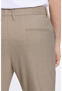 Pantaloni a quadri beige con un tessuto texturizzato, dotati di una tasca posteriore e una vestibilità su misura, che completano una linea della cintura elegante.